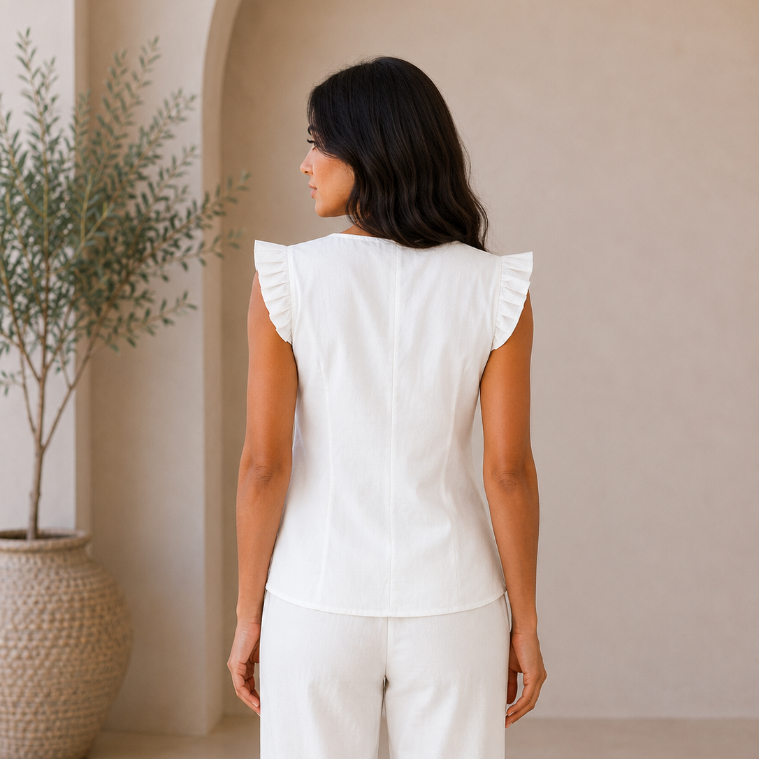 Woman wearing a white outfit standing in a minimalistic room with a plant.