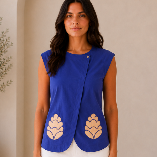 Woman wearing a blue sleeveless top with beige floral patterns against a neutral background